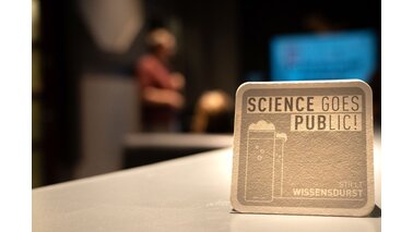 Das ist ein grauer Bierdeckel mit der Aufschrift "Science Goes Public!" 